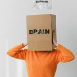 Crop person putting creased paper with Rubbish title in container with Brain inscription on head of female on light background